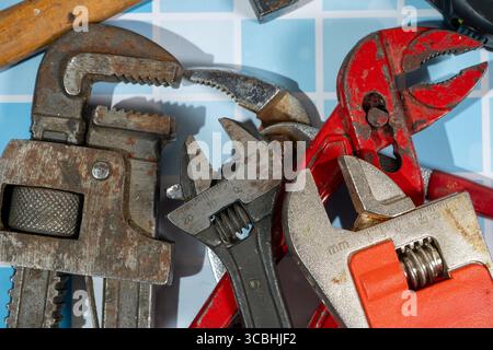 Many well-used wrenches and pipe wrench are laying on blue tiles, showing signs of wear and tear Stock Photo