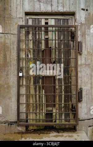 Rusty steel grid door with old broken wooden door behind on a concrete wall Stock Photo