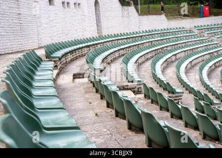 Large, open-air stone amphitheater is filled with numerous rows of green plastic seats arranged in a semi-circular pattern Stock Photo