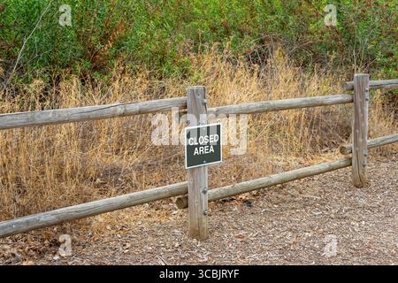 A Closed Area sign on a rail wooden fence with dry grass and green shrubs Stock Photo