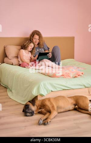 Mother and daughter using tablet on bed with sleeping dog Stock Photo