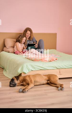 Mother and daughter using tablet on bed with sleeping dog Stock Photo
