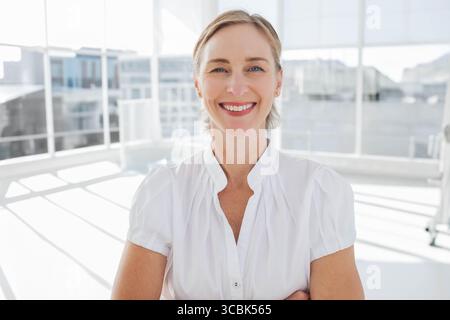 Mature adult woman in white blouse standing by office window showing sunlight reflections on floor. Professional, corporate, modern, architecture, bus Stock Photo