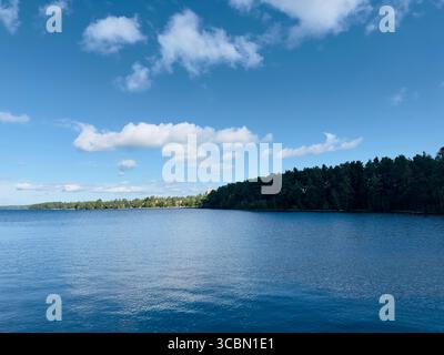 A beautiful summer day at the lake with puffy white clouds in the sky and the forest in view. Stock Photo