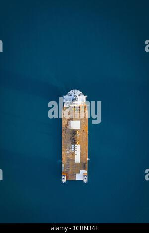 Aerial view of a large cargo ship with a white hull and brown deck cutting through the deep blue sea, Porto Venere, Liguria, Italy. Stock Photo