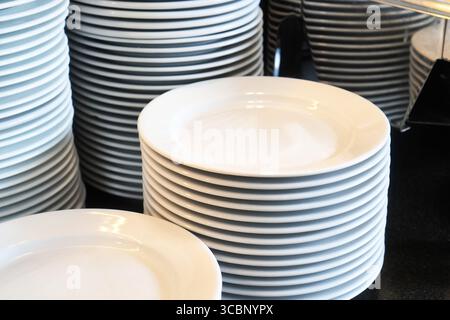 Several stacks of clean white plates arranged on a table in a restaurant. Stock Photo