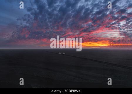 Sunset Over Black Sand Plain with Vehicles on Dirt Road in Iceland Stock Photo