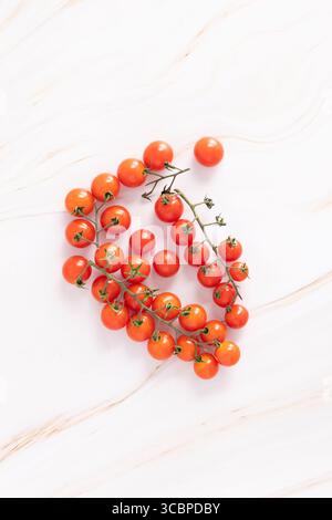 Fresh cherry tomatoes on the vine, arranged in a circular pattern on a light marble surface. Photographed from above. Stock Photo