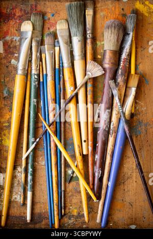 Top-down view of colorful artist paint brushes scattered across a paint-splattered wooden surface, symbolizing creativity, art tools, and the painting Stock Photo
