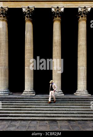 A man in a suit and hat walks down a set of stairs in front of large columns. Stock Photo