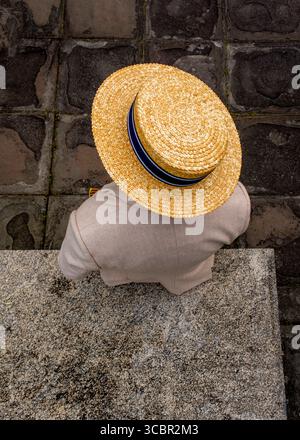 A person wearing a straw hat and a light-colored jacket is seen from above, standing on a stone surface. Stock Photo