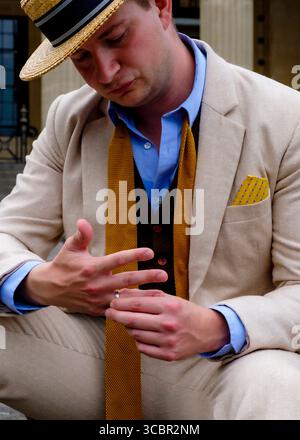 A man in a straw hat and suit is looking down at his hands, possibly adjusting a ring. Stock Photo