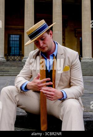 A man in a straw hat and suit is sitting down and looking at his hands. Stock Photo
