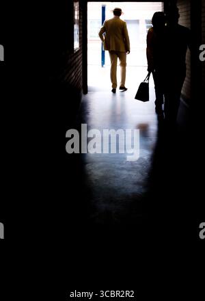 A man in a suit and hat walks away from the camera, while two people walk towards the camera in the dark. Stock Photo