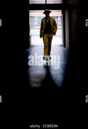 A man in a suit and hat walks towards the camera in a dark hallway. Stock Photo
