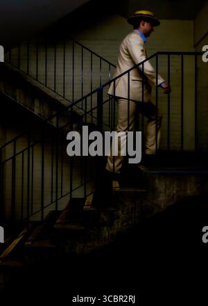 A man in a suit and hat is walking up a flight of stairs. Stock Photo