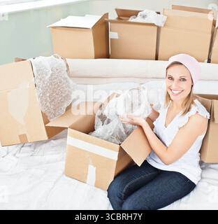 Woman holding glass jar with bubble wrap on white couch among moving boxes, copy space Stock Photo