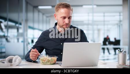 Busy Businessman Enjoys Healthy Lunch While Working On Computer At Office. Stock Photo