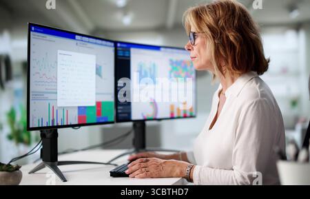 Elderly Woman Consulting Financial Charts From Home Computer For Analysis Stock Photo