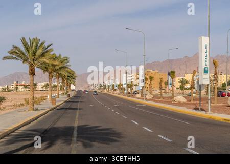 Scenic Highway 80 winds through Aqaba outskirts, Jordan, with desert sands and Middle Eastern mountains rising in the distance under clear daylight. Stock Photo