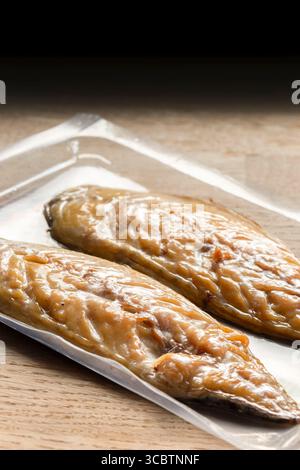 Smoked mackerel fillets vacuum packed in plastic packaging. On a wooden chopping board background. Stock Photo