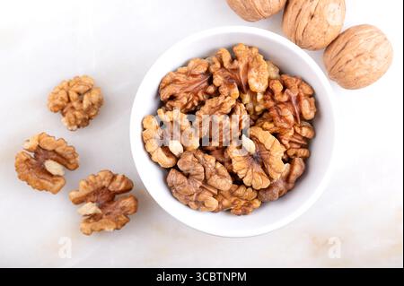 Walnut kernel halves, in a white bowl, on a marble surface. Shelled and dried halves of walnut kernels, seeds of common walnut tree, Juglans regia. Stock Photo