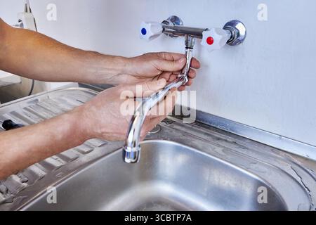Mounting new sink faucet with straight spout while plumber aligns plumbing parts for proper installation in modern kitchen sink. Stock Photo