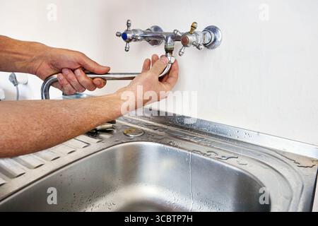 Disassembly of kitchen faucet displays hands separating long spout from faucet body above sink basin while sink faucet remains mounted on kitchen sink Stock Photo