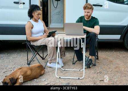 Freelancers working remotely outside their camper van with dog Stock Photo