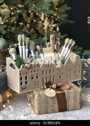 Christmas-themed setup featuring a gift box wrapped in music sheet paper with a decorative holder filled with paintbrushes. The scene is set against a Stock Photo