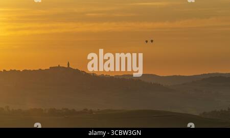 Hot air balloons float above Tuscan hills at sunrise with golden light Stock Photo