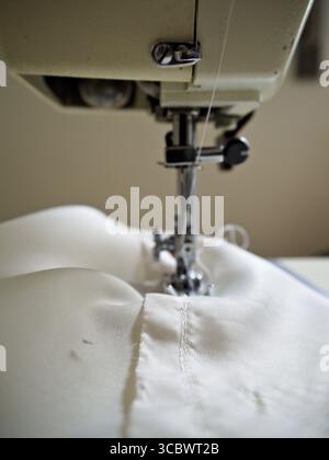 Industrial sewing machine stitching white fabric, close-up of needle and seam in textile manufacturing. Stock Photo