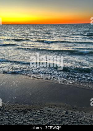 Sunset gradient from blue to orange above blue ocean water with small waves. Stock Photo