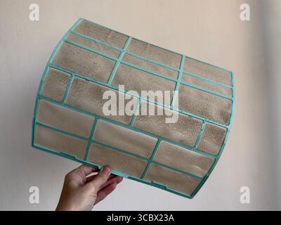 Extremely dusty and clogged AC filter held in hand on white background, symbol of poor air quality and need for cleaning Stock Photo
