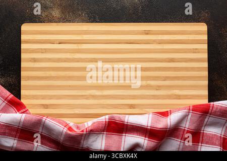 New rectangular bamboo wooden cutting board on stone background with red striped towel. Top view. Mock up for food project Stock Photo