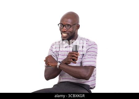 young man wearing optical glasses sitting on chair with mobile phone and doing cross gesture with his arms while smiling. Stock Photo