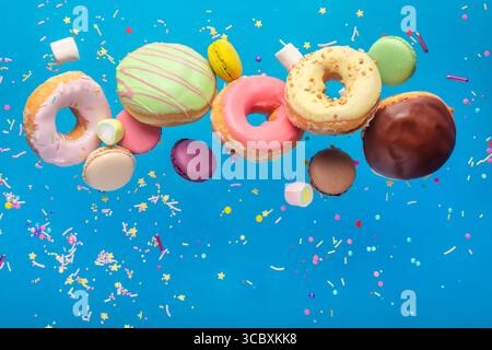 Tasty colorful donuts with macaroons and sprinkles flying against blue background. Celebration concept Stock Photo