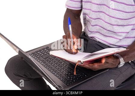 hands of a young man taking notes in a notebook using a laptop. Stock Photo