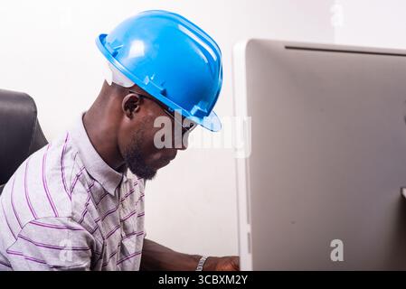 young man engineer wearing blue safety helmet sitting at desk. Stock Photo