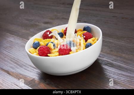 Pouring milk in corn flakes with fresh berries, on wooden background Stock Photo
