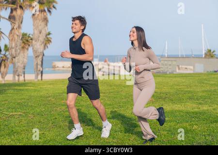 Fit couple jogging together on seaside lawn, smiling and chatting Stock Photo