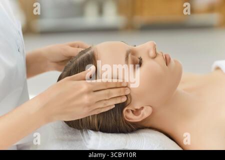 Beautiful dark haired woman has facial massage, feeling relaxed, keeping eyes closed Stock Photo