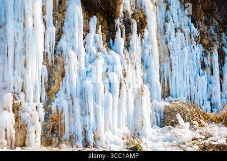 Majestic frozen waterfall with long icicles on a rocky cliff in winter. Stock Photo