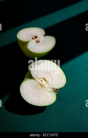 Minimalist composition of a fresh green apple cut in half, placed on a deep green surface with dramatic shadows. Stock Photo
