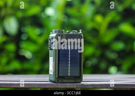 VINKOVCI, CROATIA, 06.13.2025:A portable outdoor radio with a built-in solar panel sits on a wooden surface with a blurred greenery background, illust Stock Photo