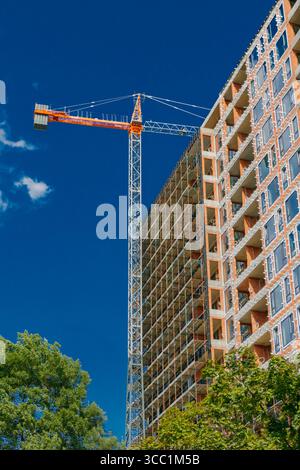 Workers are busy at a construction site as a crane hoists materials to the upper floors of a high-rise building surrounded by green trees in bright af Stock Photo