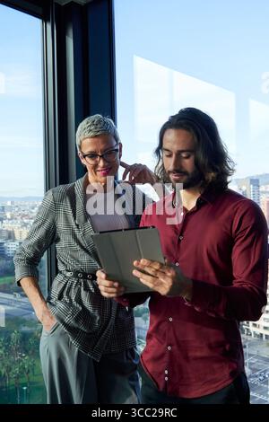 Businesspeople using tablet, working together in modern office with city view. Stock Photo