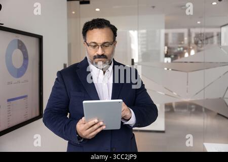 Mature businessman focused on online work on pad in boardroom Stock Photo