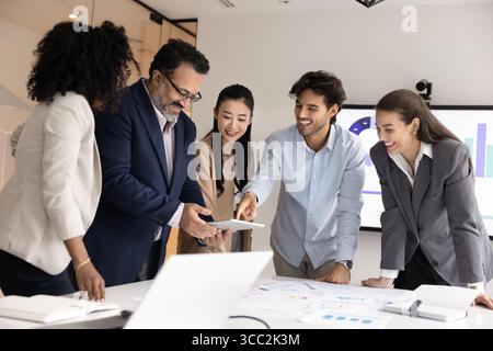Joyful international analysts group work on project using digital tools Stock Photo