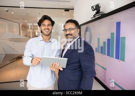Two businessmen look at camera with happy smiles holding tablet Stock Photo